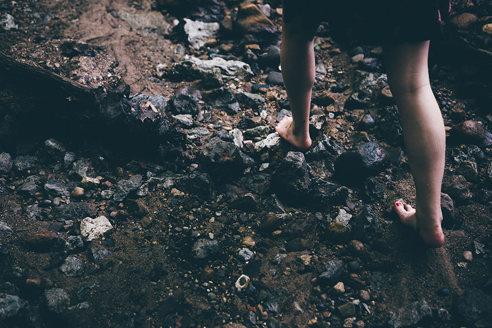 A woman walking over rocks with bare feet.