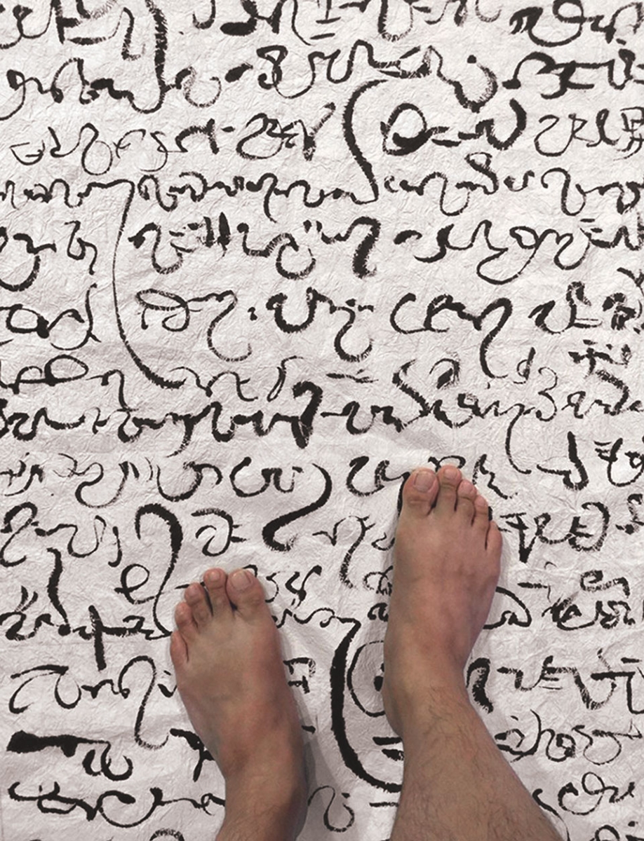 Bared feet standing on a cloth covered in a non-English script.