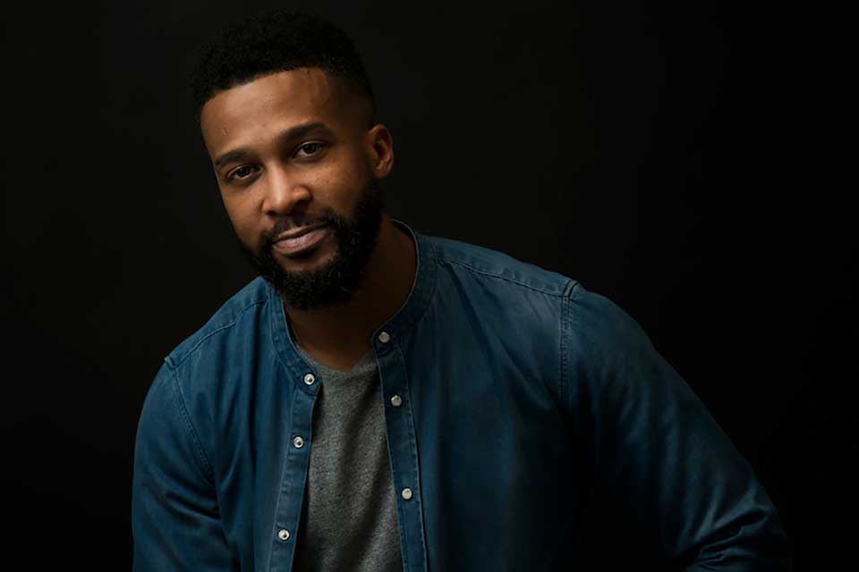 A photograph of Clemonce Heard posing in front of a dark background in low light