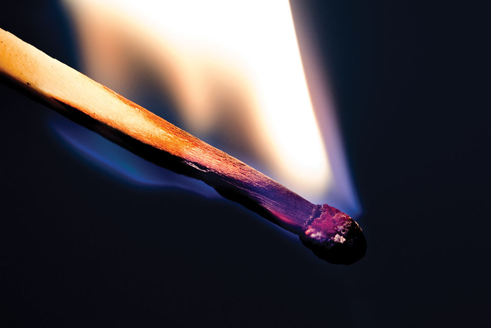 A close-up photograph of a wood match burning