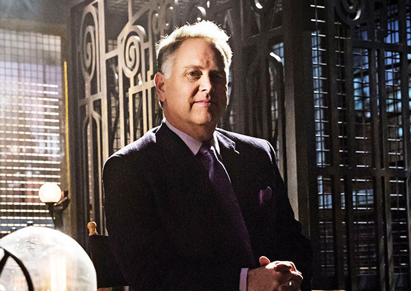 A man in a suit stands in front of an antique style open elevator