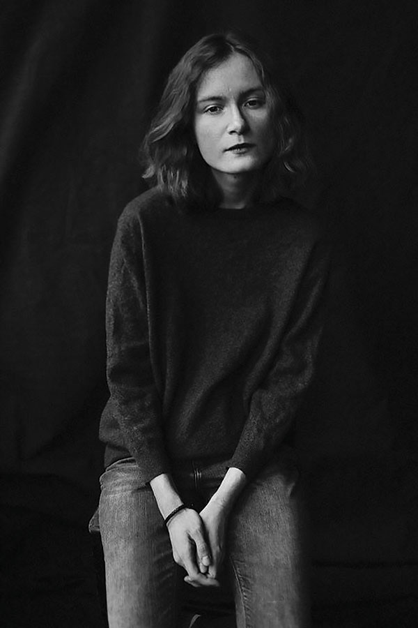 A black and white photo of a woman in a dark sweatshirt and black jean looking at the camera