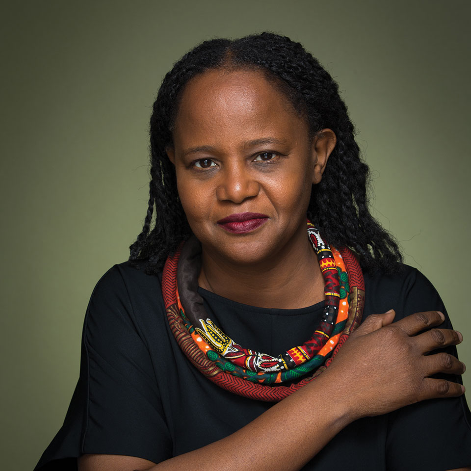 A photograph of Edwidge Danticat, wearing black offset by a colorful scarf, against an olive background