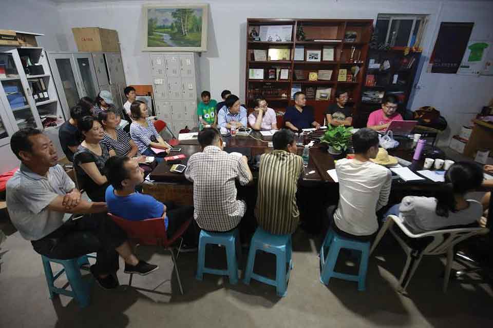 A group of people sit around a table, many of them looking toward the head of the table