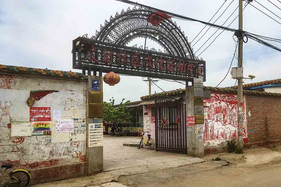 A wrought-iron gate stands open between two shambolic stone walls, adorned with graffiti