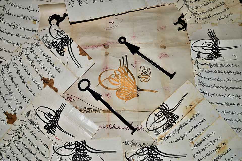 Pieces of paper, covered in Arabic writing, are scattered on a table. A pair of keys sits near the center