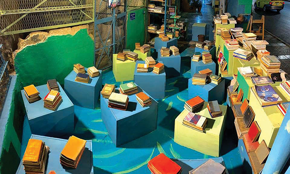 An aerial shot of a warehouse type space, the floor covered with colored boxes with stacks of books on them