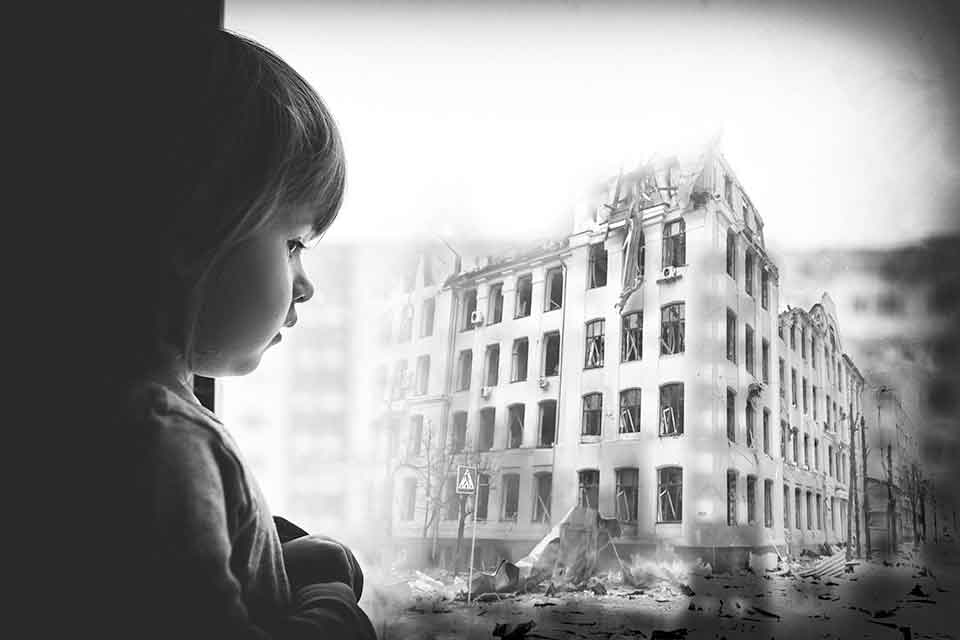 A black and white photograph of a child looking through a frosted window at a battle-damaged building across the street