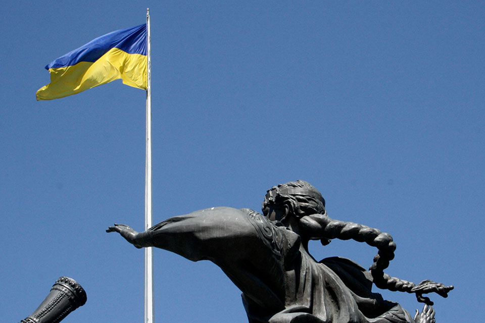 A metal sculpture of a woman looking up at the flag of Ukraine