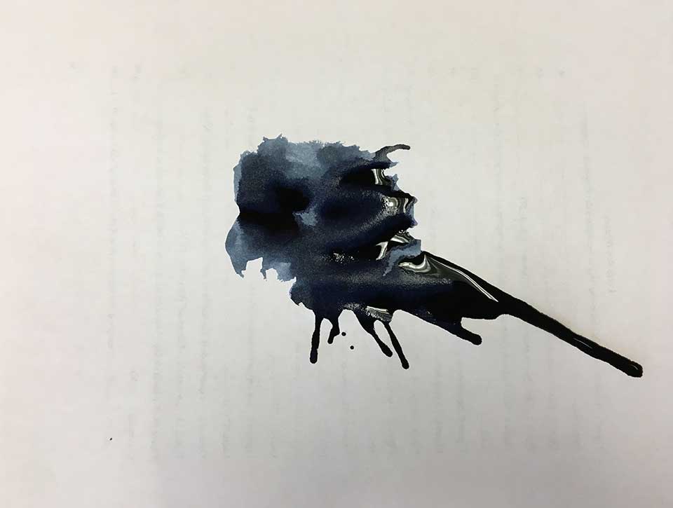 A large inkblot stain on white paper, through which writing on the opposite side just just be seen but not read