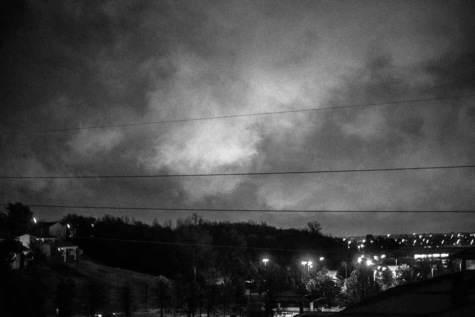 A black and white photograph of a hill, silhouetted against the growing dusk