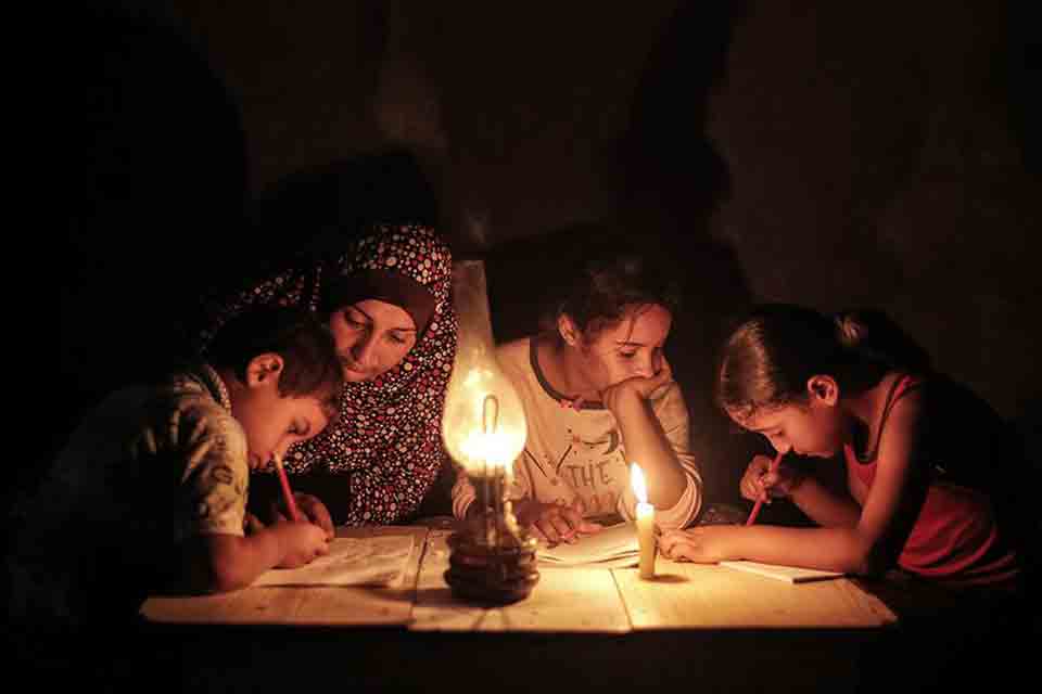 A family huddles around a makeshift table, doing schoolwork by candlelight