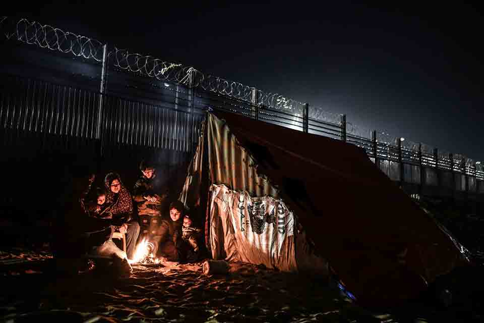 A family camps in the shadow of a highly fortified wall at night