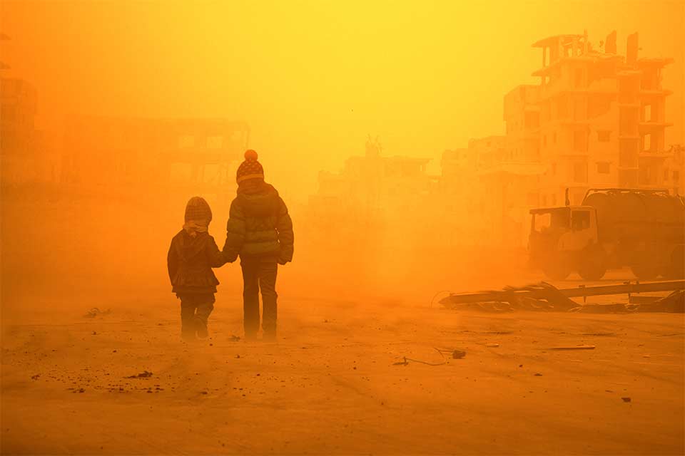 Two children wearing winter coats walking through an orange, smoggy landscape