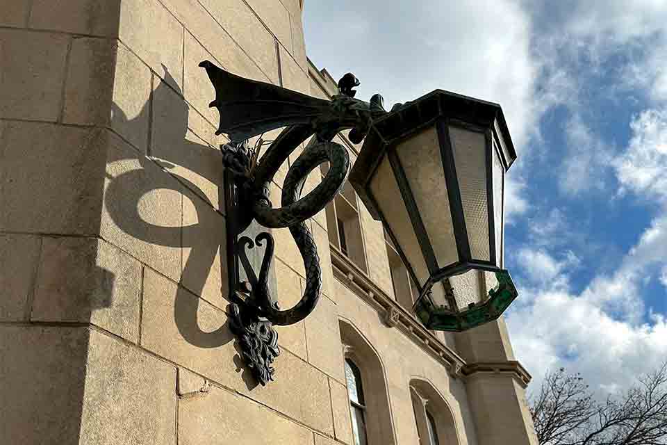 A wrought-iron lamp holder with a glass lamp hanging off the side of a stone. building