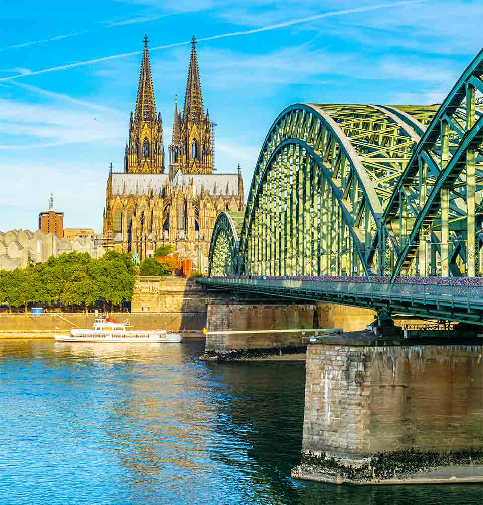 An ornate metal bridge spans a river leading to a cathedral