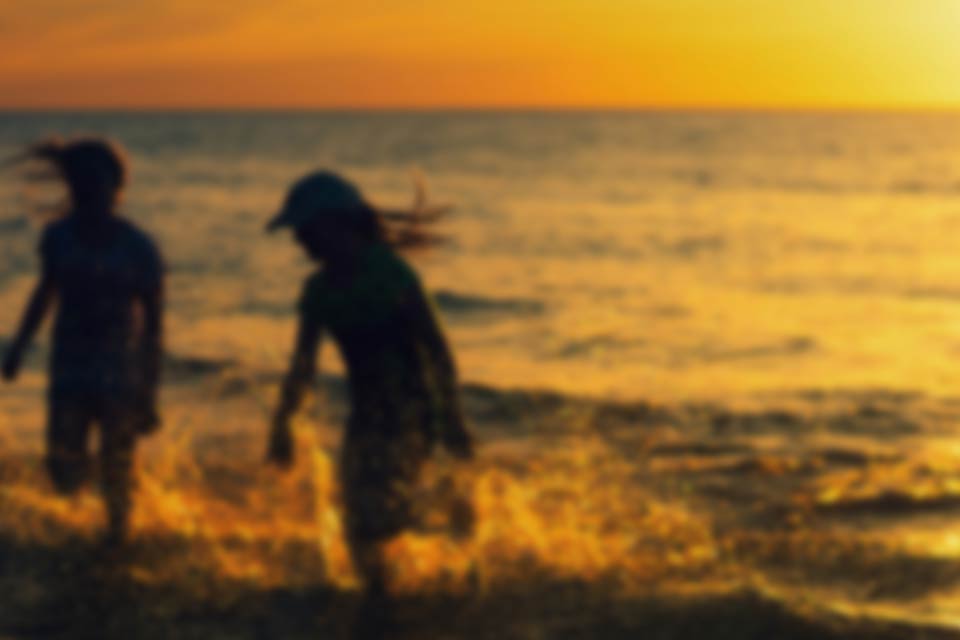 A gauzy photograph of two children playing in the surf. The sun is setting and they are mostly swallowed in shadow