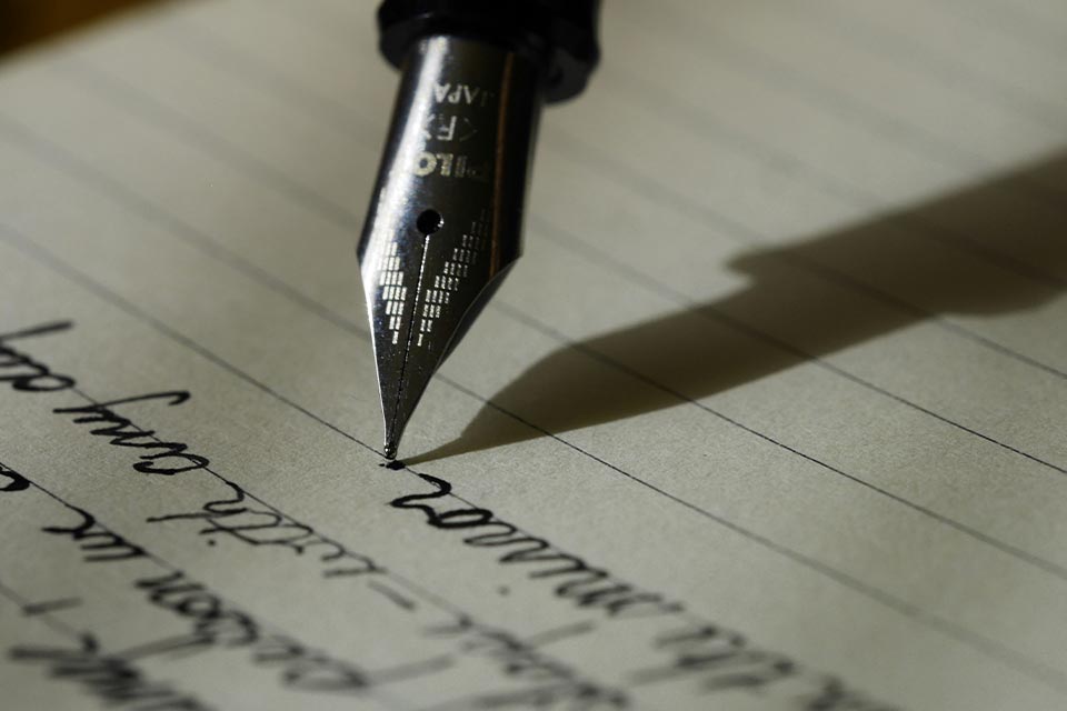 A pen hovers above lined paper with words (text unimportant) preceding