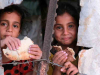 Two children eating bread peer through a crack in a ruined structure