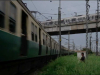 A man wades through a grassy field to approach a train in the city.