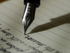 A pen hovers above lined paper with words (text unimportant) trailing behind