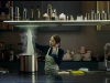 A woman stands in a shadowy kitchen cooking