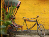 A bicycle connected to a carriage, parked in front of a mustard-colored brick wall