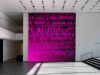 Ghostly electronic words inhabit a dark magenta canvas in a white museum hall