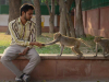 A man sits in an urban park. He has stretched out his hand to a monkey nearby. Another monkey watches then.