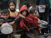 A woman cues up with two children, each holding a metal basin amid a crowd of refugees