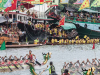 A photograph of a raucous public festival where teams of rowers in dragon boats traverse a river