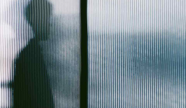 A human figure in silhouette through opaque textured glass