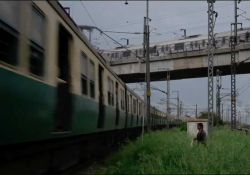 A man wades through a grassy field to approach a train in the city.