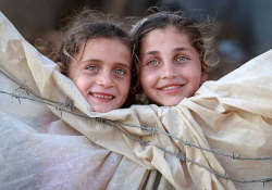 Two children peer out of a canvas tent 