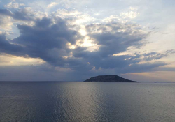 An island, shrouded in darkness, a light can be seen on the sea surrounding peeking in from the edges