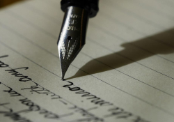 A pen hovers above lined paper with words (text unimportant) trailing behind