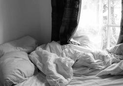 An unamde bed, bathed in light from a nearby window