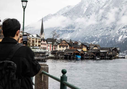A person stands on the outskirts of an Alpine city taking a photo of it with his phone