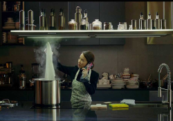 A woman stands in a shadowy kitchen cooking