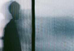 A human figure in silhouette through opaque textured glass