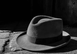 A man's hate sits partially illuminated by sunlight on a table.