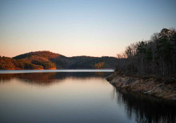 A placid lake at sunset with grassy land jutting out into it.