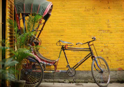 A bicycle connected to a carriage, parked in front of a mustard-colored brick wall