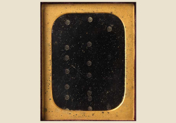 An abstract image of a black field with circles embossed into it, framed by gold. The image is set against a cream background.