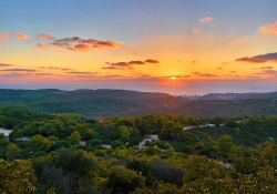 A photograph of an idyllic river valley with the sun rising in the background