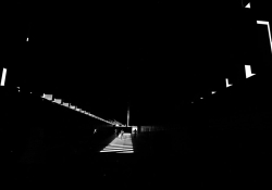 A photograph of the interior of the The National Memorial for Peace and Justice, mostly swallowed in darkness with a small path lit in the center and small slits visible on the walls