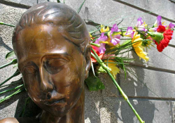 A photograph of a the head of a bronze statue of a female figure. Flowers have been placed behind the statue's head