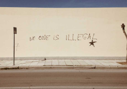 A photograph of a wall with the words, "No one is illegal" spray painted on it