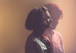 Beth Porter stands in the center of the frame, facing right as Ben Please stands just behind her, partially obscured