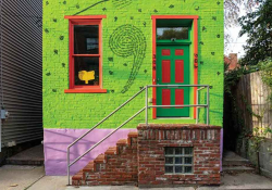 A photograph of a house, painted green, with an comma painted between window and door